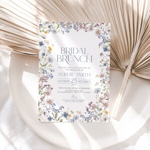 May include: A floral-themed bridal brunch invitation with a white background and a border of watercolor flowers in shades of blue, pink, and green. The text reads "Bridal Brunch" in a blue font, followed by "Please join us in honor of the bride-to-be Sophie Smith" and "Saturday 25 December 20XX". The invitation also includes the time and location of the event, as well as the RSVP information.