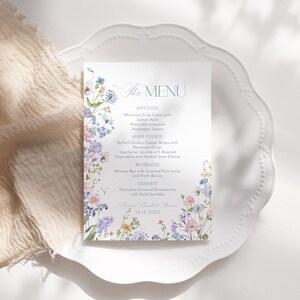 K&ouml;nnte beinhalten: Eine florale Hochzeitsmen&uuml;karte mit einem Aquarelldesign mit blauen, rosa und gelben Blumen. Das Men&uuml; umfasst Vorspeisen, Hauptgericht, Getr&auml;nke und Desserts. Der Text lautet "The Menu" und enth&auml;lt das Datum "14.12.20XX".