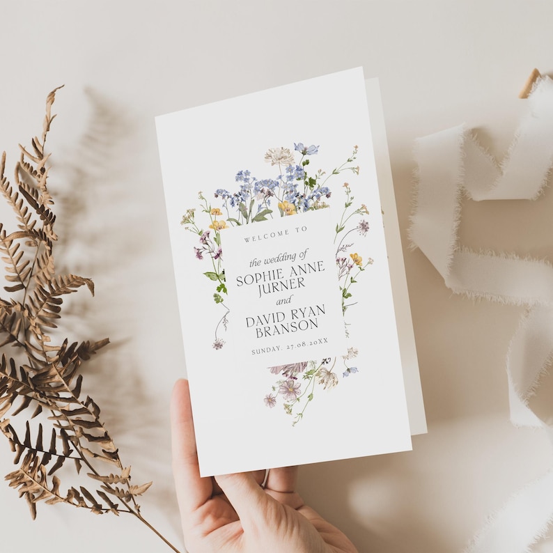 May include: A white wedding program card featuring a watercolor illustration of blue, yellow, and purple wildflowers. The text reads: WELCOME TO the wedding of SOPHIE ANNE JURNER and DAVID RYAN BRANSON SUNDAY, 27.08.20XX.