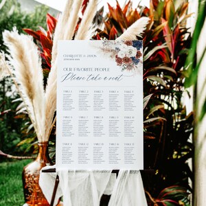 May include: A white wedding seating chart with a floral design in shades of blue, red, and white. The chart lists tables 1 through 15 with guest names. The text reads "Charlotte & Jason 27th June 20XX Our Favorite People Please Take a Seat."