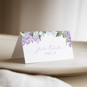 May include: Lilac floral wedding place card with the name "Julia Roberts" and the text "Table 01" printed on it.