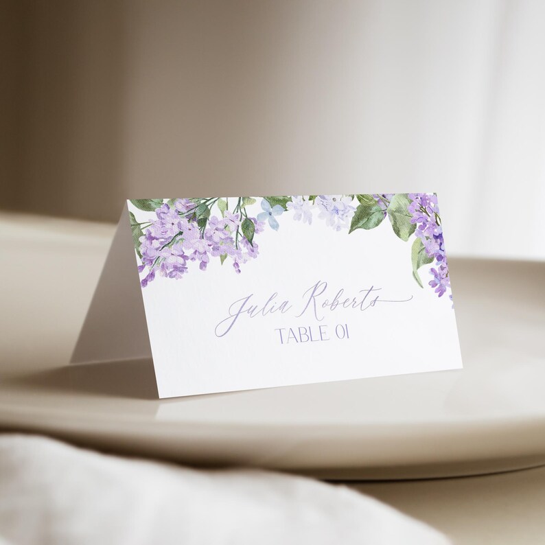 May include: Lilac floral wedding place card with the name "Julia Roberts" and the text "Table 01" printed on it.