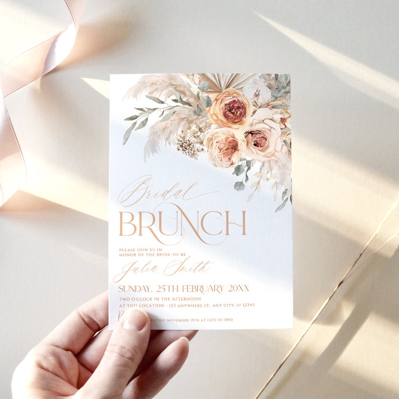 May include: A white rectangular invitation card featuring a floral arrangement of pampas grass and roses in shades of peach and cream. The text reads Bridal Brunch, Please join us in honor of the bride-to-be, Julia Smith, Sunday, 25th February 20XX.