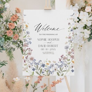 May include: A white wedding welcome sign with a floral border. The sign reads "Welcome to the wedding of Sophie Hooper and David Robert 08|10|20XX 123 Anywhere St, Any City, ST 12345".