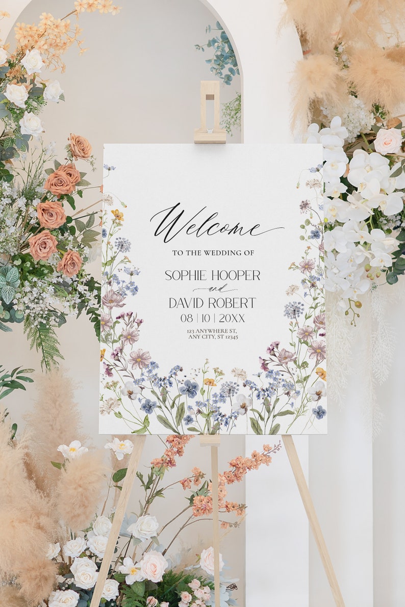 May include: A white wedding welcome sign with a floral border. The sign reads "Welcome to the wedding of Sophie Hooper and David Robert 08|10|20XX 123 Anywhere St, Any City, ST 12345".