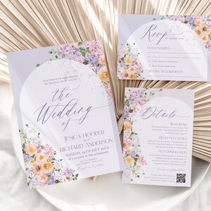 May include: A set of wedding invitation cards with a floral design. The cards are printed on a light purple background with a white circle in the center. The text on the cards is in a purple font. The cards are decorated with watercolor flowers in shades of pink, purple, and yellow.