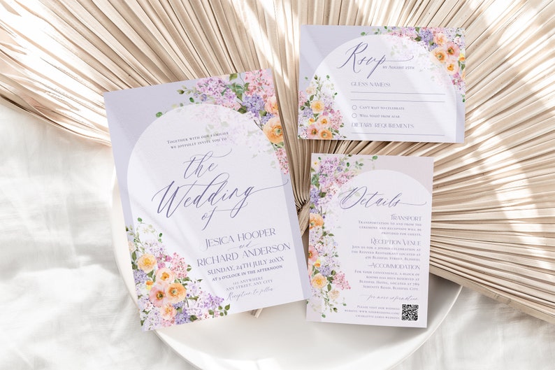 May include: A set of wedding invitation cards with a floral design. The cards are printed on a light purple background with a white circle in the center. The text on the cards is in a purple font. The cards are decorated with watercolor flowers in shades of pink, purple, and yellow.