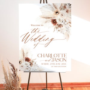 May include: A white wedding welcome sign on a black metal easel featuring brown cursive text that reads Welcome to the Wedding of Charlotte and Jason, Sunday, 27th June 20XX, at this location, decorated with dried pampas grass and flowers.