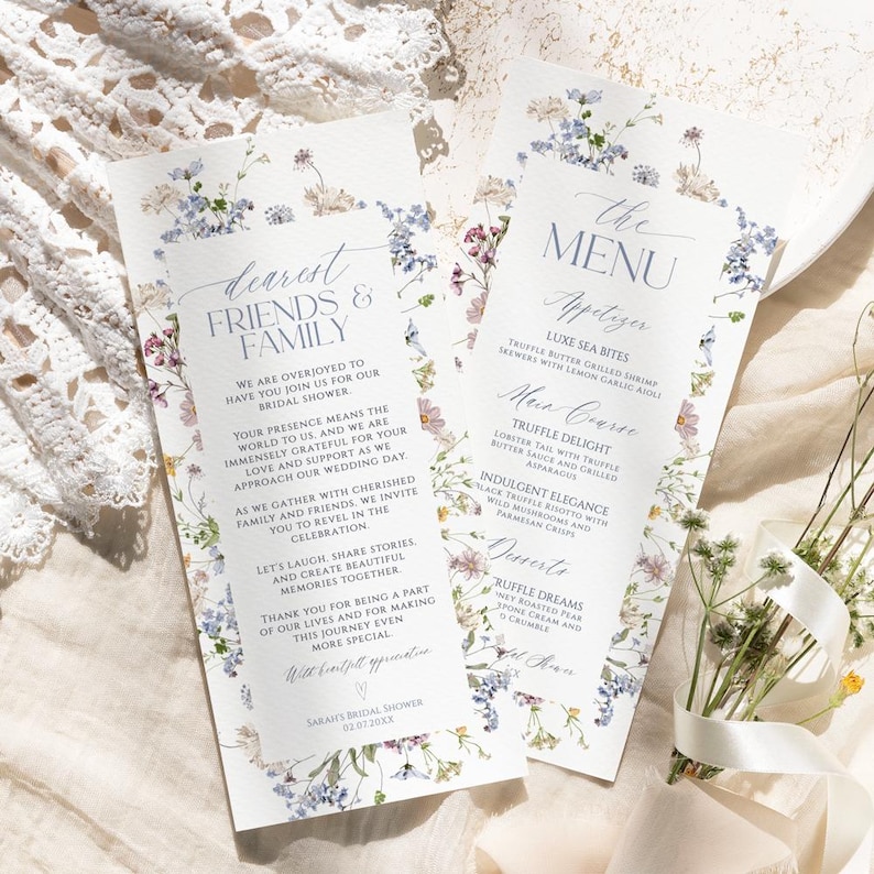 Puede incluir: Dos tarjetas de papel rectangulares con un borde floral de flores silvestres azules, rosas y amarillas. Una tarjeta dice Dearest Friends & Family, la otra The Menu, enumerando platos para una fiesta nupcial.