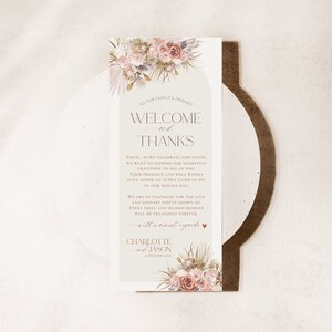 May include: A welcome and thank you sign for a wedding with a floral design in shades of pink, beige, and green. The text reads "Welcome and Thanks" with a message expressing gratitude to guests for their presence and well wishes. The sign is signed "Charlotte & Jason".