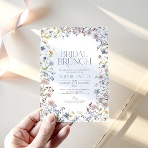 May include: A floral-themed bridal brunch invitation with a watercolor design. The invitation features a light blue background with a white border. The text reads "Bridal Brunch" in a light blue font. The invitation also includes the bride-to-be's name, the date of the event, and the time and location. RSVP information is included at the bottom.