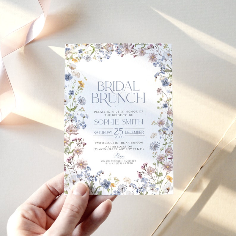 May include: A floral-themed bridal brunch invitation with a watercolor design. The invitation features a light blue background with a white border. The text reads "Bridal Brunch" in a light blue font. The invitation also includes the bride-to-be's name, the date of the event, and the time and location. RSVP information is included at the bottom.