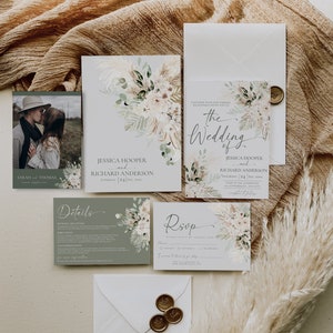 May include: A wedding stationery set featuring a photo card of a couple, an invitation, a details card, and an RSVP card. The cards are decorated with watercolor pampas grass and floral illustrations in muted green and beige tones.