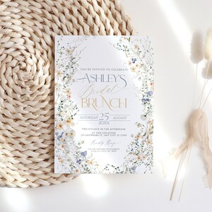 May include: A floral-themed bridal brunch invitation with a white background and blue and yellow flowers. The text reads "You're invited to celebrate Ashley's Bridal Brunch, Saturday 25 August 20XX, Two o'clock in the afternoon at this location 123 Anywhere St. Any City, ST 12345, RSVP on or before November 15th at (123) 45 7890."