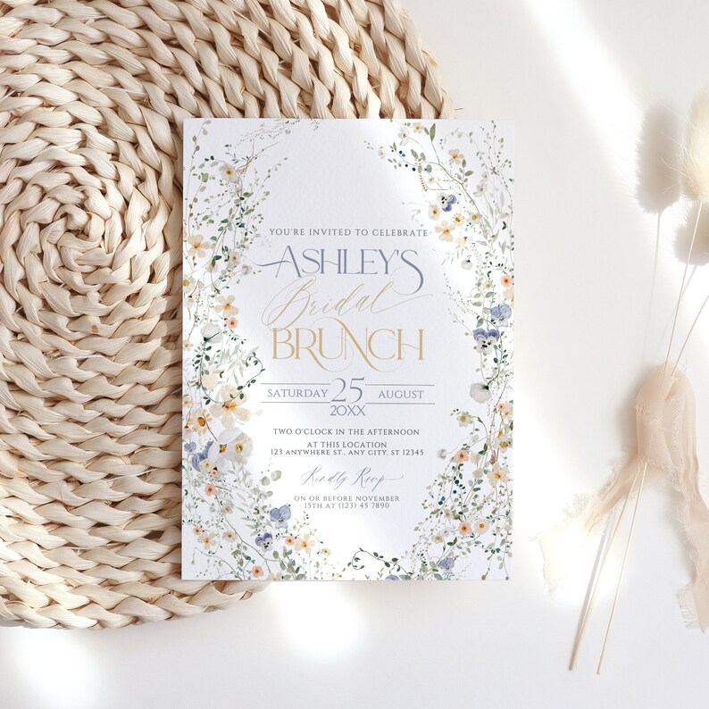 May include: A floral-themed bridal brunch invitation with a white background and blue and yellow flowers. The text reads "You're invited to celebrate Ashley's Bridal Brunch, Saturday 25 August 20XX, Two o'clock in the afternoon at this location 123 Anywhere St. Any City, ST 12345, RSVP on or before November 15th at (123) 45 7890."
