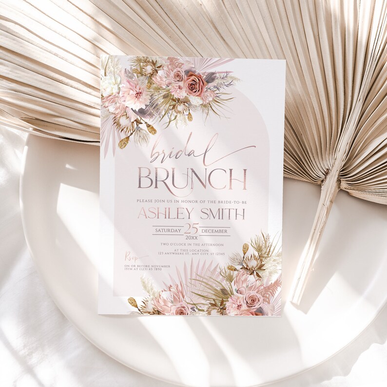 May include: A blush pink and gold bridal brunch invitation with a floral design. The invitation reads "bridal brunch" and includes the bride-to-be's name, Ashley Smith, the date, Saturday, December 25, 20xx, and the time, two o'clock in the afternoon. The invitation also includes the location, 123 Anywhere St, Any City, 31 12148. The RSVP information is on the bottom of the invitation.