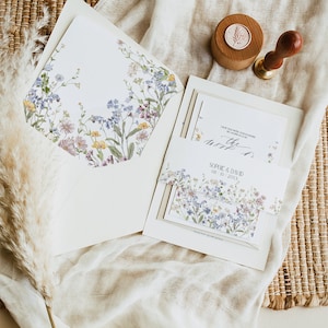 May include: A wedding invitation suite with a floral design. The invitation is white with a border of blue and pink flowers. The envelope is white with a floral design. The text on the invitation reads "Save the Date" and "Sophie & David" with the date "08.10.20XX".