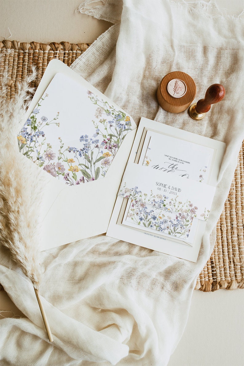 May include: A wedding invitation suite with a floral design. The invitation is white with a border of blue and pink flowers. The envelope is white with a floral design. The text on the invitation reads "Save the Date" and "Sophie & David" with the date "08.10.20XX".