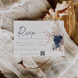 Op de afbeelding: Een rechthoekige RSVP-kaart met donkerblauwe schrijfletters en een bloemenillustratie met marineblauwe rozen en pampasgras. De kaart bevat lijnen voor namen, selectievakjes voor aanwezigheid, een QR-code en de tekst I promise to dance if you play.