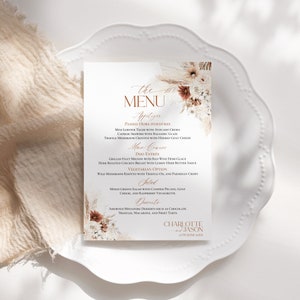 May include: A rectangular wedding menu card featuring floral illustrations in shades of cream, brown, and rust. The text includes "THE MENU," "Appetizer," "Main Course," "Vegetarian Option," "Salad," "Desserts," and "CHARLOTTE and JASON 27TH JUNE 20XX."