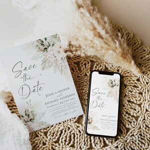May include: A save the date card with a watercolor floral design in shades of green and white. The card reads "Save the Date" with the names Jessica Hooper and Richard Anderson, the date September 24, 20XX, and the time 1 o'clock in the afternoon. The card is sitting on a woven placemat with a bouquet of dried pampas grass.