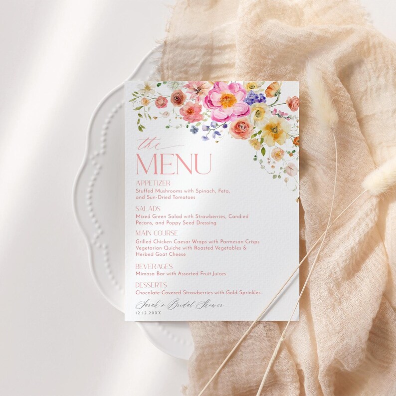Op de afbeelding: Een menukaart met een aquarel bloemenontwerp met de tekst "the MENU" in roze. Het menu bevat voorgerechten, salades, hoofdgerecht, dranken en desserts. Onderaan de kaart staat "Jane's Bridal Shower 12.12.20XX".