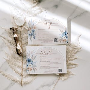 May include: Two rectangular white cards featuring blue and beige floral illustrations, an arched graphic, and text including RSVP and details. A gold metal wax seal stamp and a round white wax seal are positioned next to the cards.