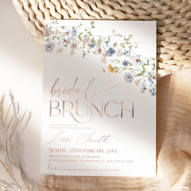 May include: A white invitation with a floral border in shades of blue and pink. The text reads "bridal brunch" in rose gold lettering. The invitation is for a bridal brunch for Liam Smith on Sunday, 25th February 20XX at 2:00 PM. The RSVP information is included at the bottom.