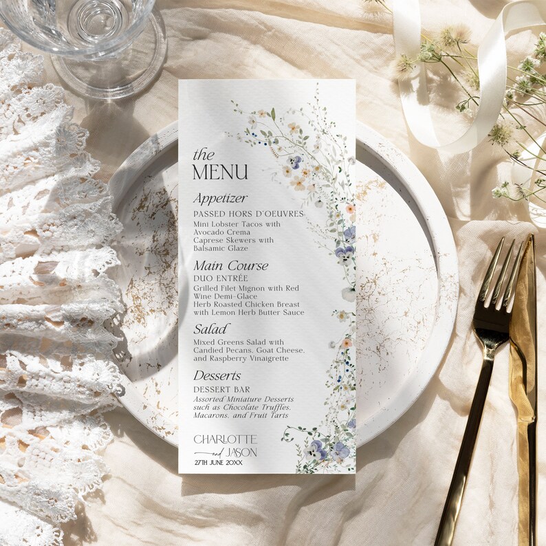 Puede incluir: Una tarjeta de men&uacute; de boda con un dise&ntilde;o floral. El men&uacute; incluye aperitivos, plato principal, ensalada y postres. La tarjeta est&aacute; decorada con delicadas flores azules y blancas y vegetaci&oacute;n. El texto en la tarjeta dice "the MENU", "Appetizer", "Main Course", "Salad", "Desserts", "CHARLOTTE and JASON", y "27TH JUNE 20XX".