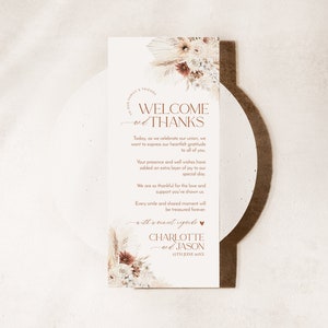 May include: A rectangular wedding thank you card featuring dried floral arrangements at the top and bottom. The text reads: Welcome and Thanks, followed by a message of gratitude, and concludes with the names Charlotte and Jason, dated 25th June 20XX.