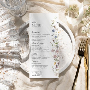 K&ouml;nnte beinhalten: Eine Hochzeitsmen&uuml;karte mit floralem Design. Das Men&uuml; umfasst Vorspeisen, Hauptgericht, Salat und Desserts. Die Karte ist auf strukturiertem Papier mit goldfarbenem Rand gedruckt. Der Text auf der Karte lautet: "the MENU, Appetizer, PASSED HORS D'OEUVRES, Mini Lobster Tacos with Avocado Crema, Caprese Skewers with Balsamic Glaze, Main Course, DUO ENTR&Eacute;E, Grilled Filet Mignon with Red Wine Demi-Glace, Herb Roasted Chicken Breast with Lemon Herb Butter Sauce, Salad, Mixed Greens Salad with Candied Pecans, Goat Cheese, and Raspberry Vinaigrette, Desserts, DESSERT BAR, Assorted Miniature Desserts such as Chocolate Truffles, Macarons, and Fruit Tarts, CHARLOTTE & JASON, 27TH JUNE 20XX"