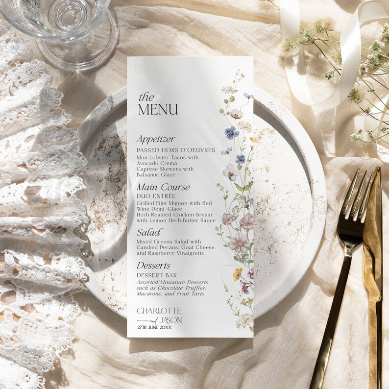 K&ouml;nnte beinhalten: Eine Hochzeitsmen&uuml;karte mit floralem Design. Das Men&uuml; umfasst Vorspeisen, Hauptgericht, Salat und Desserts. Die Karte ist auf strukturiertem Papier mit goldfarbenem Rand gedruckt. Der Text auf der Karte lautet: "the MENU, Appetizer, PASSED HORS D'OEUVRES, Mini Lobster Tacos with Avocado Crema, Caprese Skewers with Balsamic Glaze, Main Course, DUO ENTR&Eacute;E, Grilled Filet Mignon with Red Wine Demi-Glace, Herb Roasted Chicken Breast with Lemon Herb Butter Sauce, Salad, Mixed Greens Salad with Candied Pecans, Goat Cheese, and Raspberry Vinaigrette, Desserts, DESSERT BAR, Assorted Miniature Desserts such as Chocolate Truffles, Macarons, and Fruit Tarts, CHARLOTTE & JASON, 27TH JUNE 20XX"