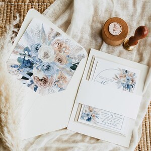 May include: A wedding invitation suite with a dusty blue and blush floral design. The invitation features a watercolor illustration of a bouquet of flowers with pampas grass. The text on the invitation reads "Saturday, 24 June 2023".
