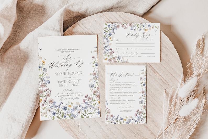 May include: Wedding invitation suite with a floral design featuring a variety of wildflowers in shades of blue, purple, pink, and yellow. The text on the cards reads "The Wedding of Sophie Hooper and David Robert 08.10.20XX Saturday at 6 o'clock in the evening at Nowhere St, Any City, ST 12345 Reception to follow".