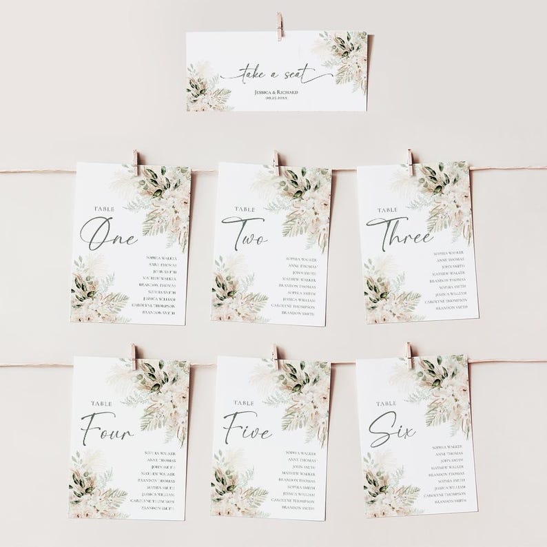 Puede incluir: Seis tarjetas de mesa con dise&ntilde;os florales y los nombres de los invitados listados en cada tarjeta. Las tarjetas est&aacute;n colgadas de una cuerda con pinzas para la ropa. La tarjeta superior dice "Take a Seat" con los nombres Jessica & Richard debajo.