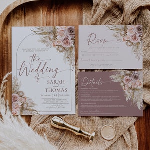 May include: A wedding invitation suite featuring a main invitation, RSVP card, and details card with floral illustrations in muted pinks and browns. A gold wax seal stamp and a circular wax seal are placed alongside the stationery.