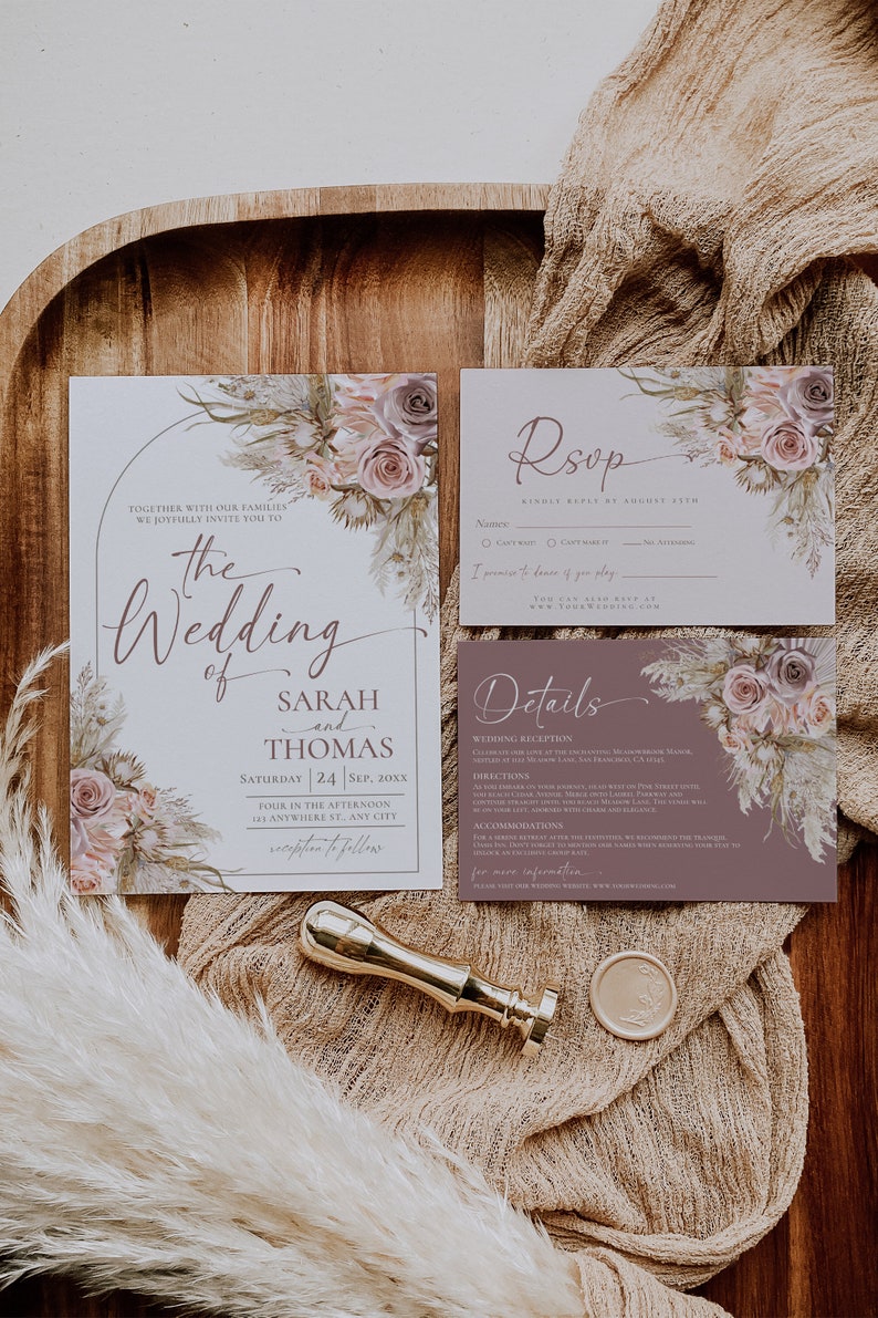 May include: A wedding invitation suite featuring a main invitation, RSVP card, and details card with floral illustrations in muted pinks and browns. A gold wax seal stamp and a circular wax seal are placed alongside the stationery.