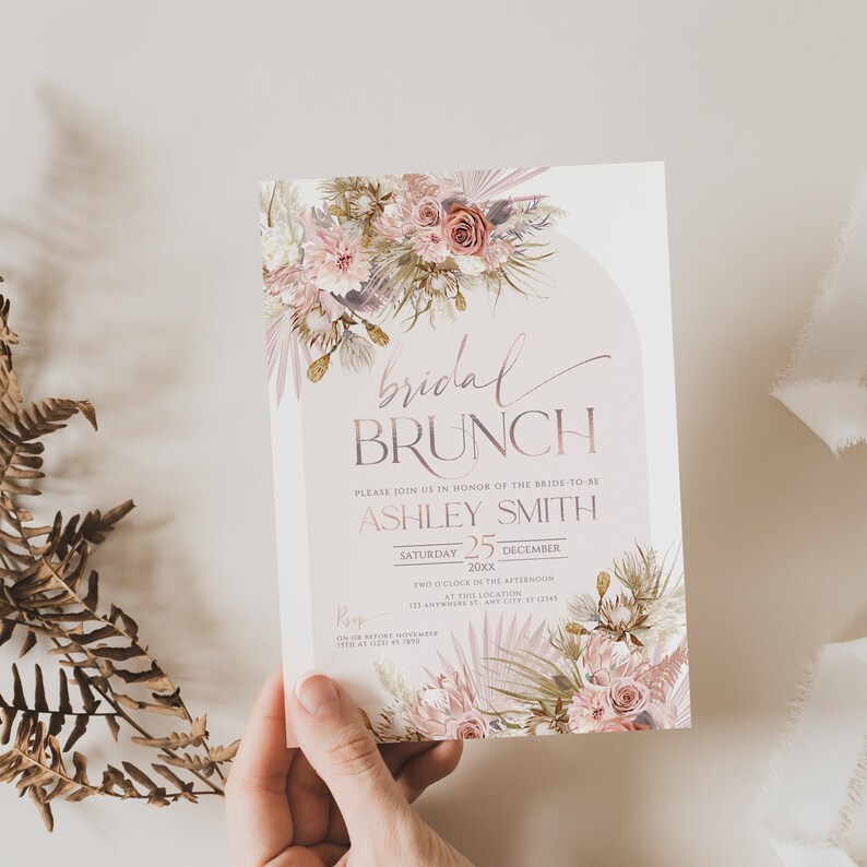 May include: A blush pink and gold bridal brunch invitation with a floral design. The invitation reads "bridal brunch" and includes the bride-to-be's name, Ashley Smith, the date, Saturday, December 25, 20xx, and the time, two o'clock in the afternoon. The invitation also includes the location, 125 Anywhere St, Any City, ST 12345, and an RSVP deadline of on or before November 15th at (123) 456-7890.