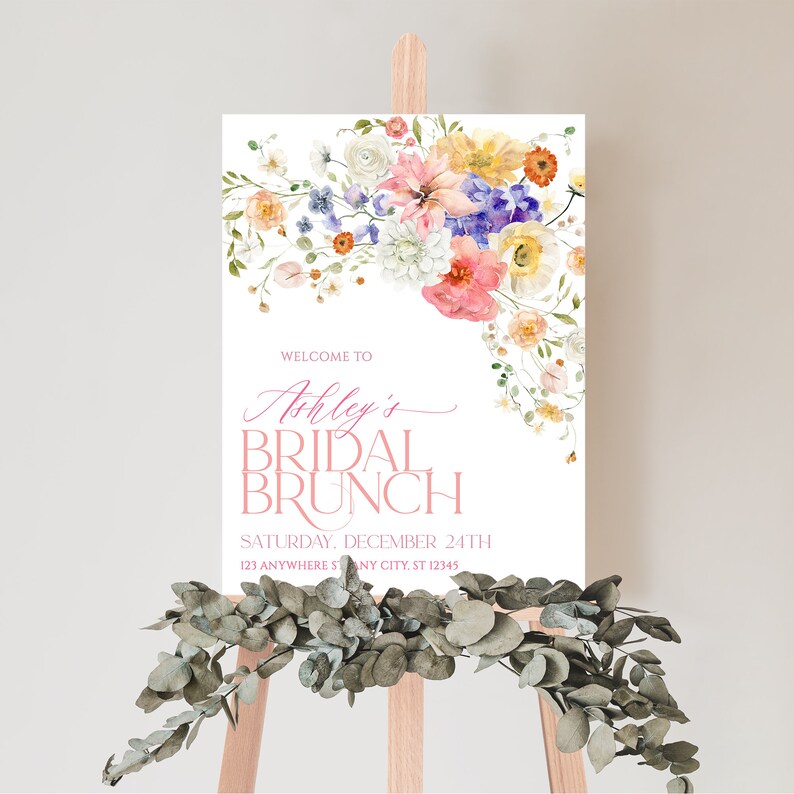 Pu&ograve; includere: Un design floreale ad acquerello con fiori rosa, gialli e blu. Il testo "Benvenuti al Brunch Nuziale di Ashley" &egrave; scritto in rosa e nero. La data "Sabato 24 dicembre" e l'indirizzo "123 Anywhere St Any City, ST 12345" sono scritti in nero.