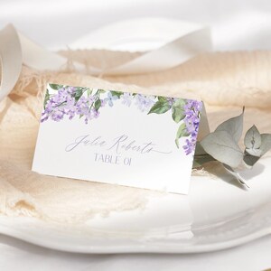 May include: Lilac floral wedding place card with the text "Julia Roberts Table 01" printed in cursive.
