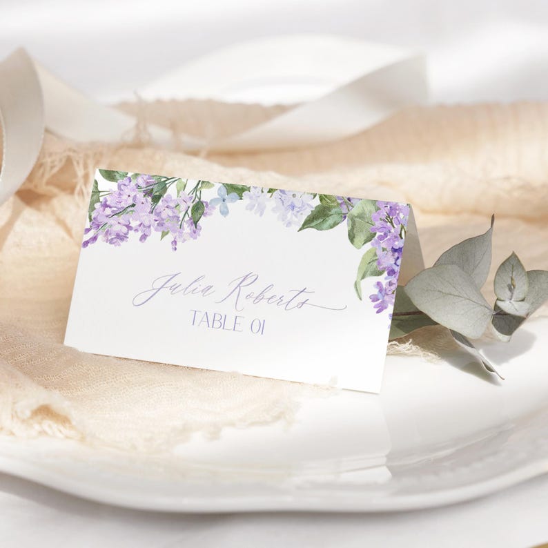 May include: Lilac floral wedding place card with the text "Julia Roberts Table 01" printed in cursive.