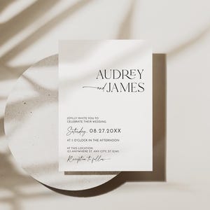 May include: A minimalist wedding invitation with the names "Audrey and James" in elegant typography. The invitation includes the date, time, and location of the wedding, with a shadow of a leaf in the background.