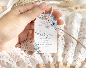 May include: A rectangular white paper tag with a hole at the top and a beige string. The tag features blue and beige floral illustrations and the text: Thank you FOR CELEBRATING WITH US with love JESSICA & RICHARD 09.25.20xx.
