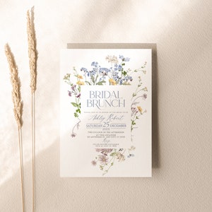 May include: A white invitation with a floral border. The text reads "Bridal Brunch" in a blue script font. The invitation is for Ashley Robert's bridal brunch on Saturday, December 25th, 20XX at 2:00 PM. The RSVP date is November 15th.