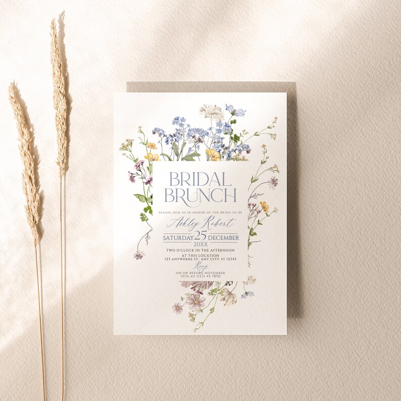 May include: A white invitation with a floral border. The text reads "Bridal Brunch" in a blue script font. The invitation is for Ashley Robert's bridal brunch on Saturday, December 25th, 20XX at 2:00 PM. The RSVP date is November 15th.