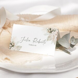 May include: White place card with a floral design and the text "Julia Roberts" and "Table 01".