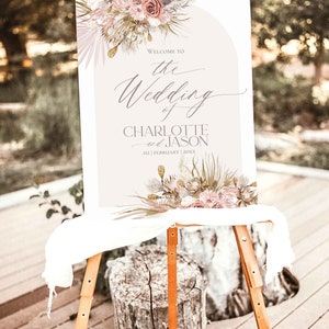 May include: A wedding welcome sign with a floral design in shades of pink, beige, and green. The sign reads "Welcome to the Wedding of Charlotte and Jason 02 | February | 20XX".