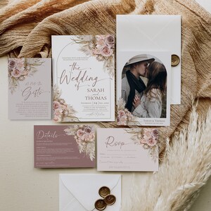May include: A wedding invitation suite featuring a main card, RSVP card, details card, and gift note. The stationery displays floral illustrations in muted pink and brown tones, elegant script typography, and a photo of a couple.