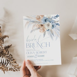 May include: A blue and white bridal brunch invitation with a watercolor floral design. The invitation includes the text "bridal brunch", "Please join us in honor of the bride-to-be", "Olivia Robert", "Saturday 25 December 20xx", "O'clock in the afternoon", and "Location - 123 Anywhere St. Any City, ST 12345".