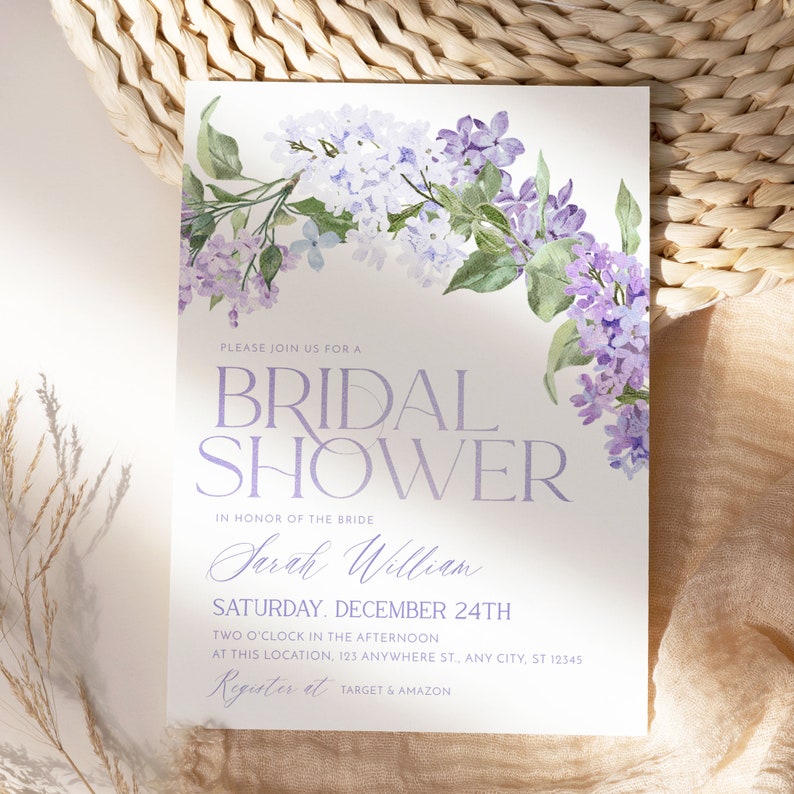 May include: A white bridal shower invitation with purple watercolor flowers in the top right corner. The text reads 'Please join us for a Bridal Shower, in honor of the bride Sarah William, Saturday, December 24th, Two o'clock in the afternoon, at this location, 123 Anywhere St., Any City, ST 12345, Register at Target & Amazon.'